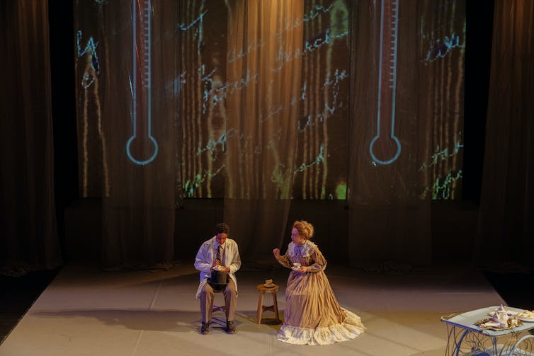 Dos actores vistos sentados en un escenario.