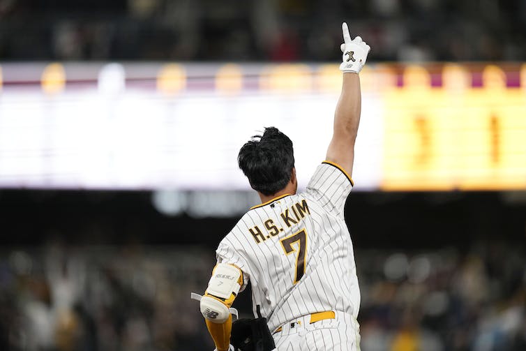 Un jugador de pelota levanta un dedo en el aire mientras corre por las bases, con las brillantes luces del estadio detrás de él.