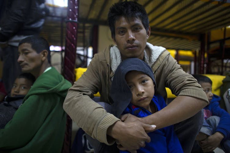 Miguel Martín y su hijo de 7 años se sientan en un refugio para inmigrantes en México mientras otros se sientan a su alrededor.