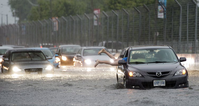 Una pierna sobresale de un automóvil que se encuentra en medio de una carretera inundada