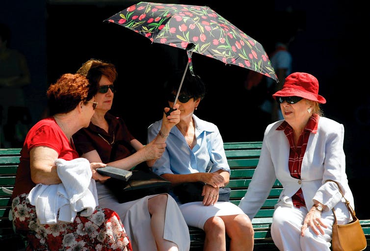 cuatro mujeres mayores que se refugian del sol bajo el paraguas
