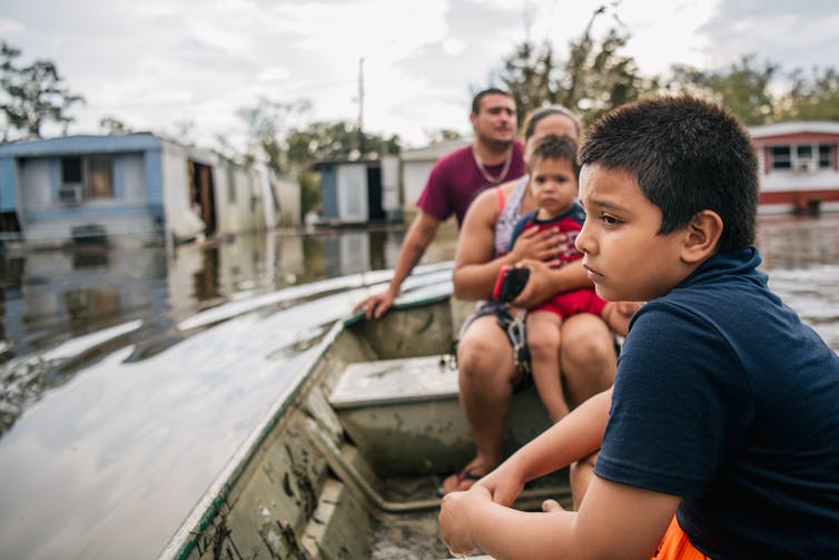 Un niño con el ceño fruncido y aspecto triste estaba sentado en un bote con su familia mientras inspeccionaban una casa móvil inundada.