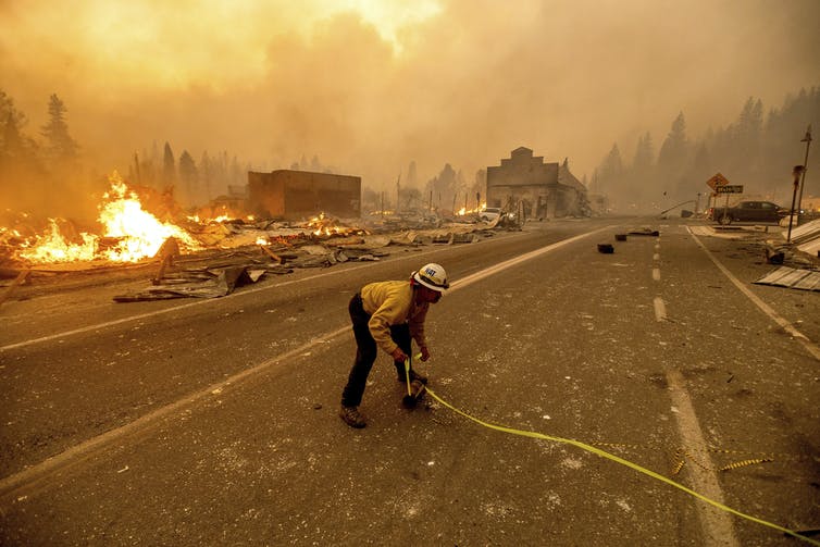 Un bombero sostiene una manguera en un camino lleno de humo