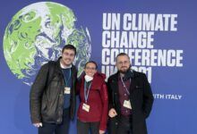 Una mujer está rodeada por dos hombres frente a un cartel de la COP26