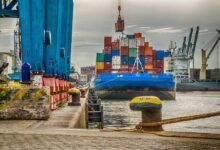 Grúas cargan contenedores en barcos atracados en el puerto.