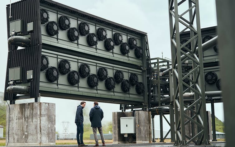 Dos hombres se paran debajo de una gran estructura con ventiladores.