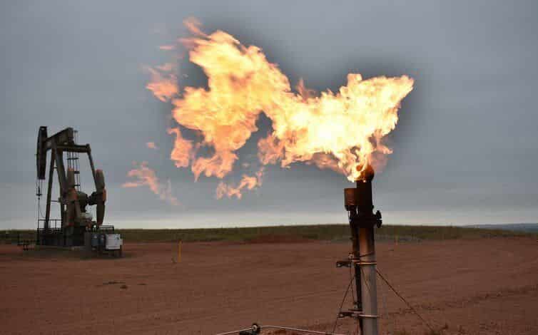Las bengalas queman gas natural en pozos de petróleo con plataformas de perforación en el fondo.