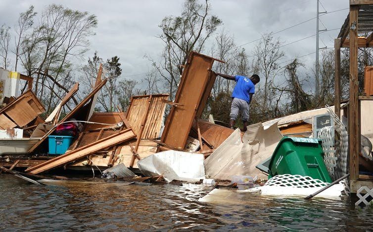 Un joven camina entre muebles y enseres domésticos esparcidos por un huracán para rescatar las pertenencias de su madre.