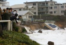 Turistas fotografían casa frente a la playa dañada por tormentas