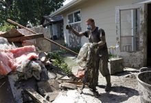 Un hombre con una máscara y guantes de trabajo arrojó escombros fangosos en una pila al lado de la casa.