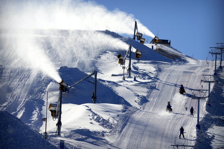 Varios barriles soplan nieve por una pista, mientras que los esquiadores usan la otra.