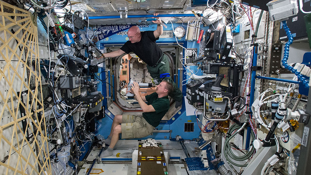 Foto de dos astronautas masculinos flotando dentro de la Estación Espacial Internacional para un examen de la vista