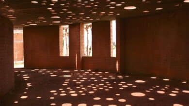 Fotografía del interior de un edificio de ladrillos de arcilla con agujeros circulares en el techo por los que se filtra la luz hasta el suelo.