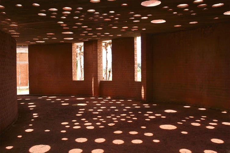 Fotografía del interior de un edificio de ladrillos de arcilla con agujeros circulares en el techo por los que se filtra la luz hasta el suelo.