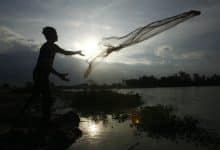Un hombre arroja una red de pesca a un cuerpo de agua contra el telón de fondo del sol naciente.