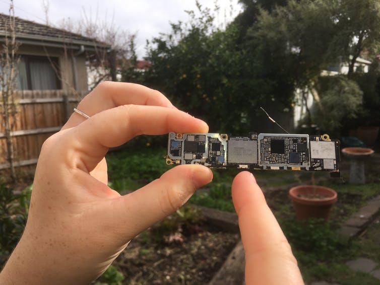 Una mano sostiene un componente del iPhone 6S y señala un pequeño chip.