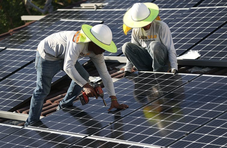 Dos trabajadores con sombreros de ala ancha instalan paneles solares en el techo