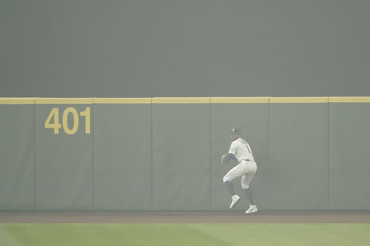 Kyle Lewis se prepara para lanzar la pelota al interior del cuadro después de atraparla mientras el humo de los incendios forestales llena el aire durante el primer partido de béisbol contra los Atléticos de Oakland, el lunes 14 de septiembre de 2020, en Seattle.
