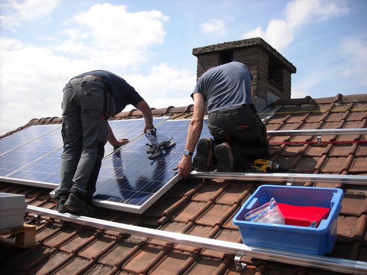 Dos personas trabajando en paneles solares en el techo.