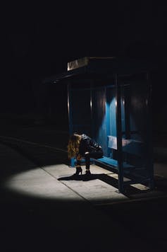 Una mujer sentada sola en una parada de autobús por la noche.