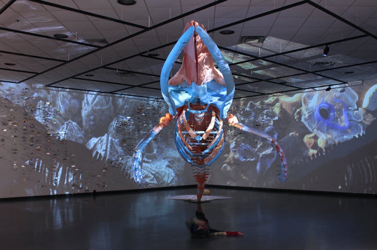 Un esqueleto de ballena hecho de plástico se muestra colgado en una habitación con imágenes proyectadas a su alrededor.