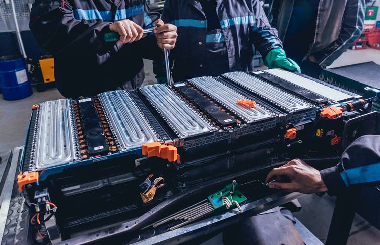 Los ingenieros se paran alrededor de una gran batería.