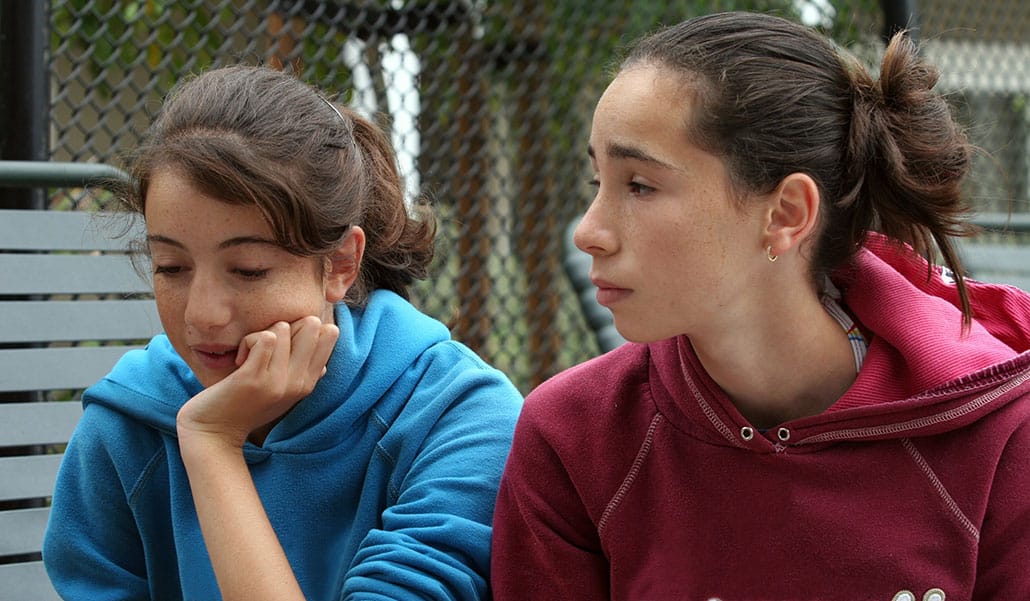 dos mujeres jóvenes con pecas, piel clara y cabello oscuro están hablando.  Una amiga está escuchando con una mirada de preocupación en su rostro.