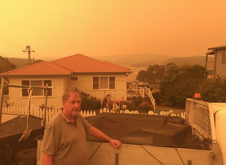 el hombre se para frente a la casa con el cielo naranja