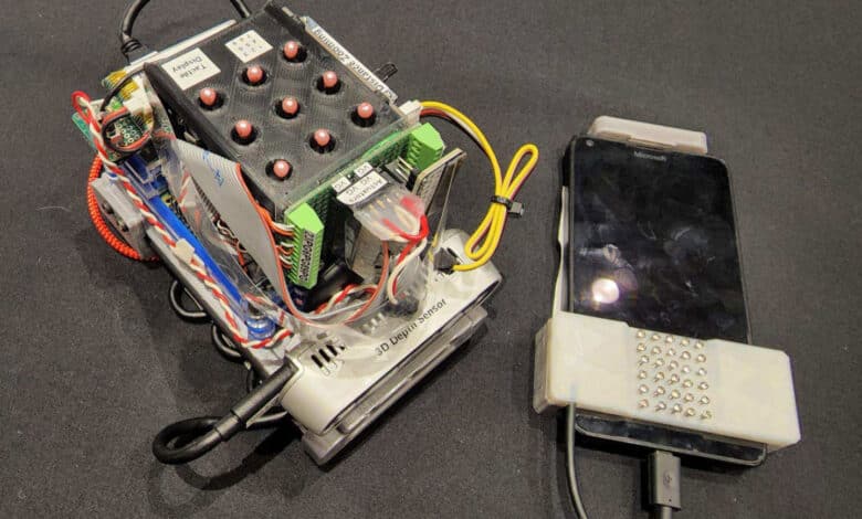 un dispositivo de mano con cables y botones se sienta en una mesa gris al lado de un teléfono inteligente