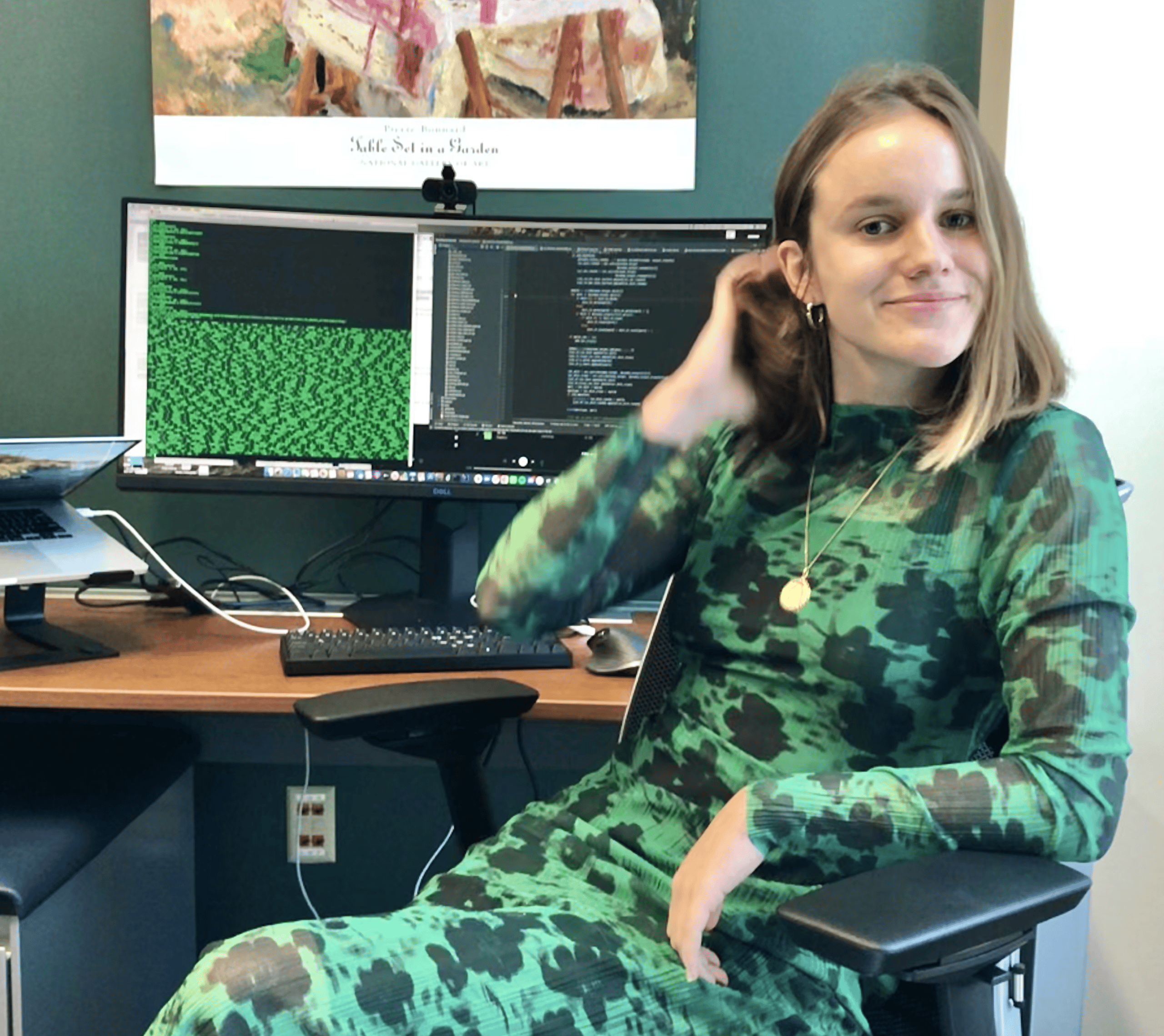 una mujer con un vestido negro y verde se sienta en un escritorio con una computadora