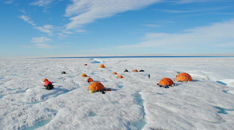 Varias tiendas de campaña de investigación de colores brillantes salpican un paisaje con arroyos y nieve en la capa de hielo.