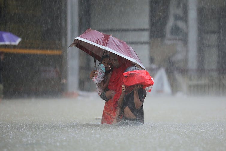 Dos niños se aferran a una mujer mientras caminan a través del agua que les llega casi hasta la cintura en una calle de la ciudad bajo una lluvia torrencial.