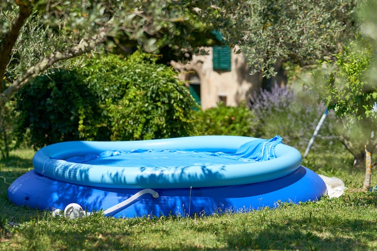 Una piscina infantil de plástico azul en un jardín con un filtro blanco adjunto.
