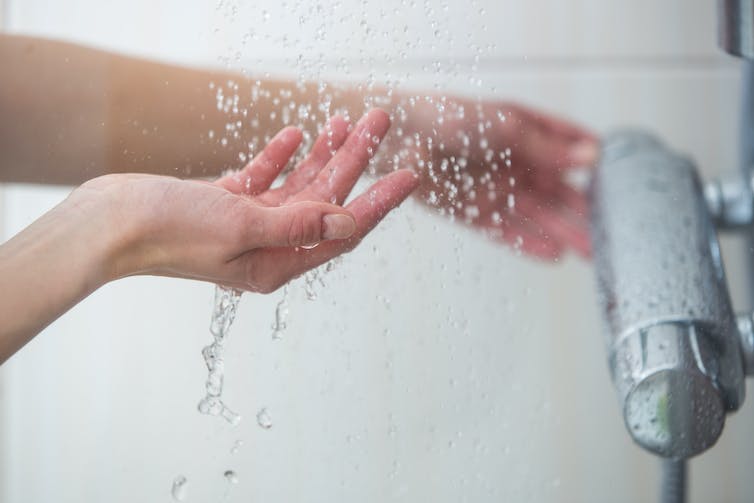 Una mano probando el agua de la ducha mientras ajusta el grifo.