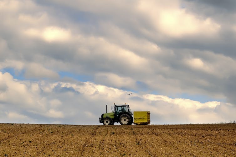 Un tractor rueda a lo largo del horizonte de un campo arado.