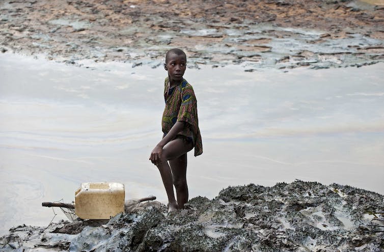 Un niño se para en la orilla de un río cubierto de aceite.