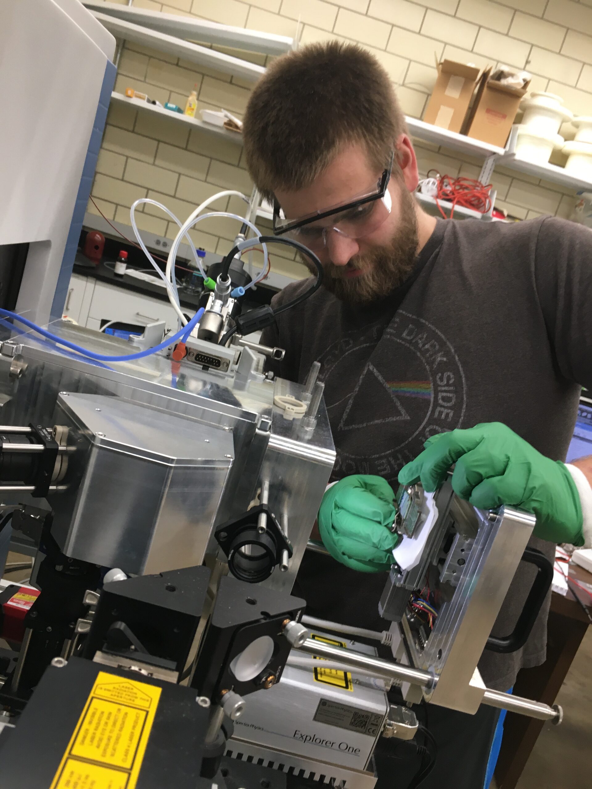 un joven con gafas y guantes trabaja en una pieza de maquinaria en un banco de laboratorio