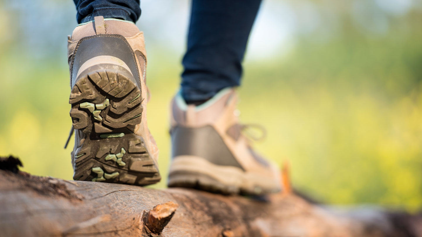 un primer plano de la parte posterior de los zapatos de alguien mientras camina por un tronco muestra la textura irregular de las suelas